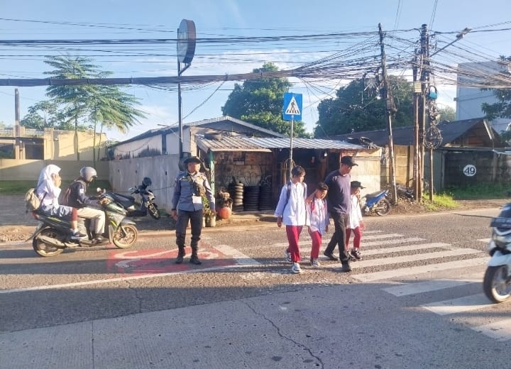 Satlinmas Tangsel saat membantu siswa menyebrang di depan sekolah.
